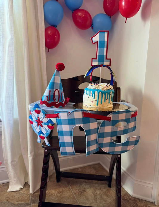 Circus themed birthday celebration setup with decorative letters on a high chair spelling the word "one", the "o" is a ferris wheel