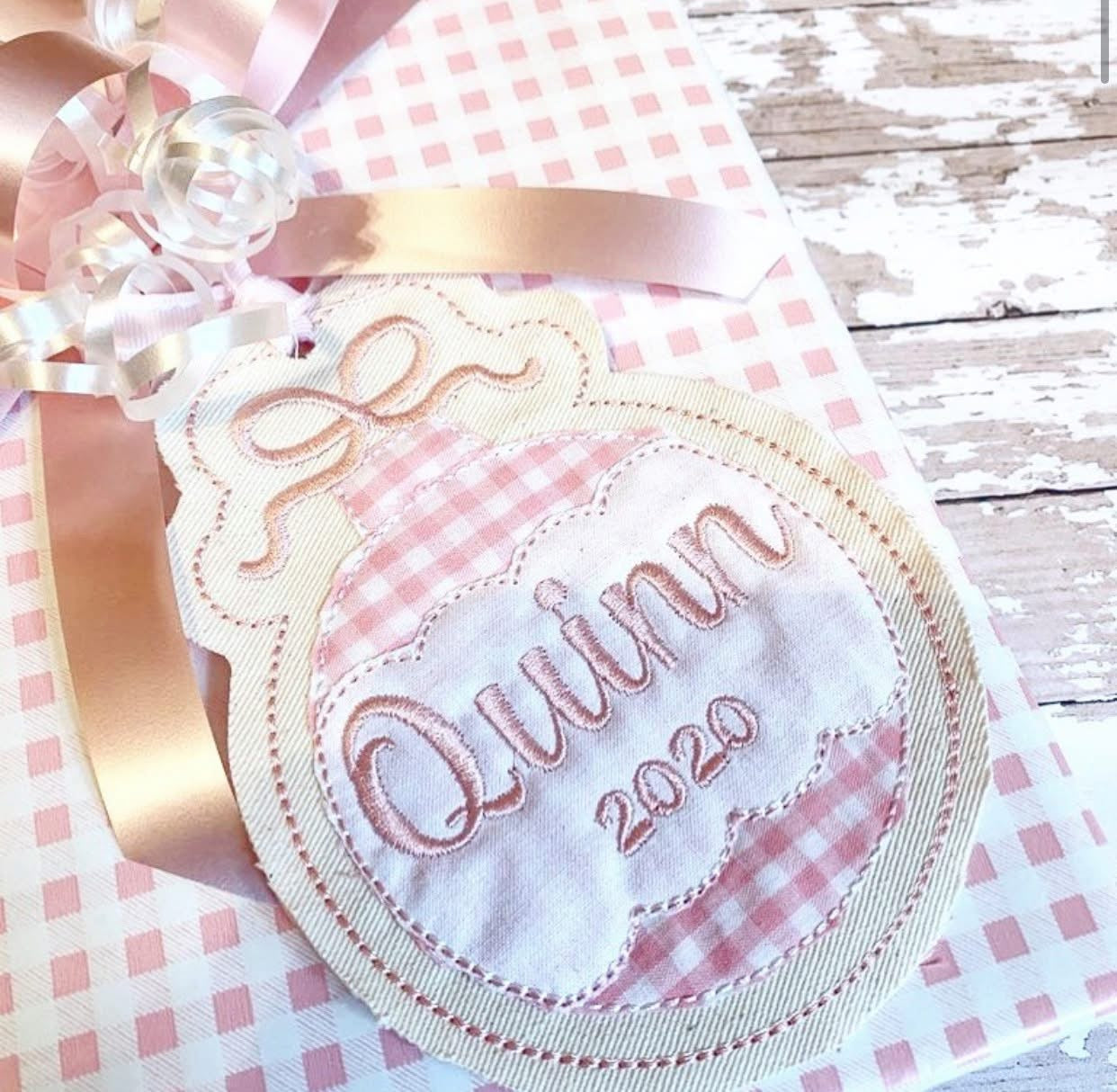 Ornament shaped gift tag with pink gingham fabric and embroidered "Quinn 2020"