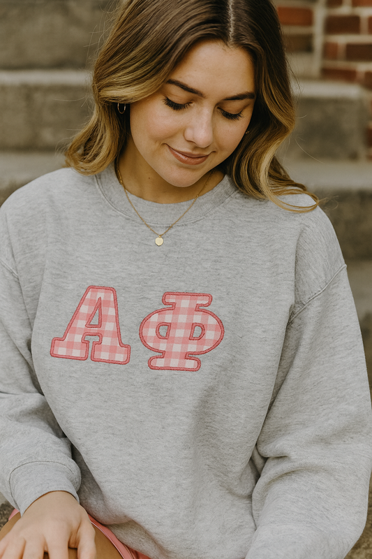 Woman wearing a gray sweatshirt with 'Alpha Phi' letters